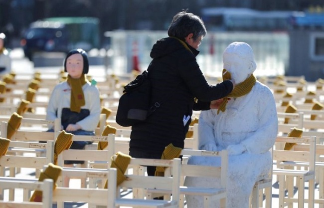 In this Wednesday, Dec. 27, 2017, file photo, a woman puts a scarf on a statue of a comfort woman sitting in a installation of empty chairs symbolizing the victims in Seoul, South Korea. (AP