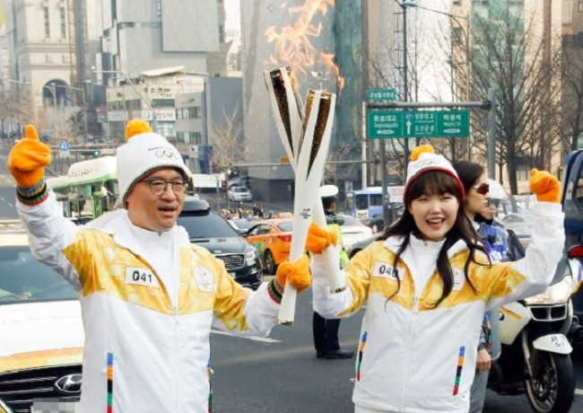 Park Hyun-jong, CEO of BHC Chicken, left, and AKMU's Lee Su-hyun carries the PyeongChang 2018 Torch in Sinsa-dong, Seoul on Monday. (Yonhap)
