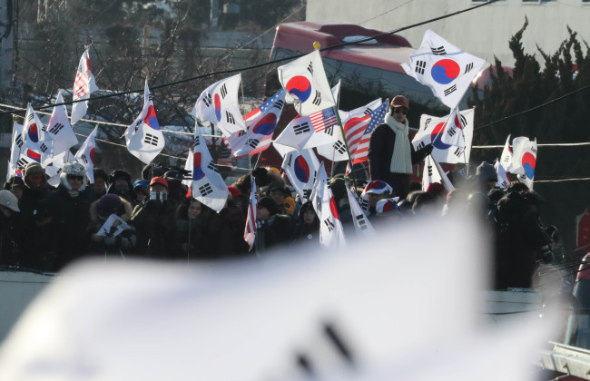 South Korean conservatives opposing the North's participation in the PyeongChang Winter Olympics wave national flags of South Korea and the US at the eastern port of Mukho on Feb. 6, 2018. (Yonhap)
