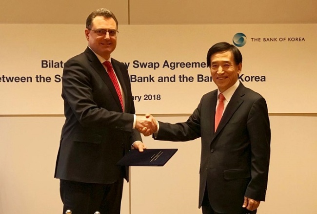 Bank of Korea (BOK) Gov. Lee Ju-yeol (R) shakes hands with Thomas Jordan, chairman of the Swiss National Bank's governing board, after signing a bilateral currency swap deal on Feb. 20, 2018, in this photo provided by the BOK. (Yonhap)