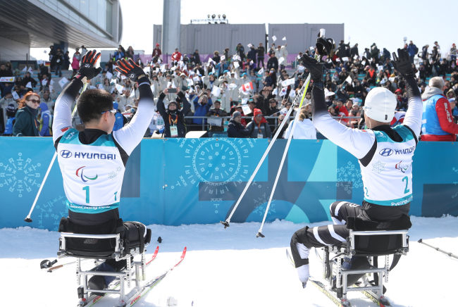 North Korea's Kim Jong-hyon (L) andMa Yu-chol respond to spectators at Alpensia Biathlon Centre in PyeongChang, some 180 kilometers east of Seoul, after they finished the men's 15-kilometer sitting cross-country skiing event at the PyeongChang Winter Paralympics on March 11, 2018. (Yonhap)
