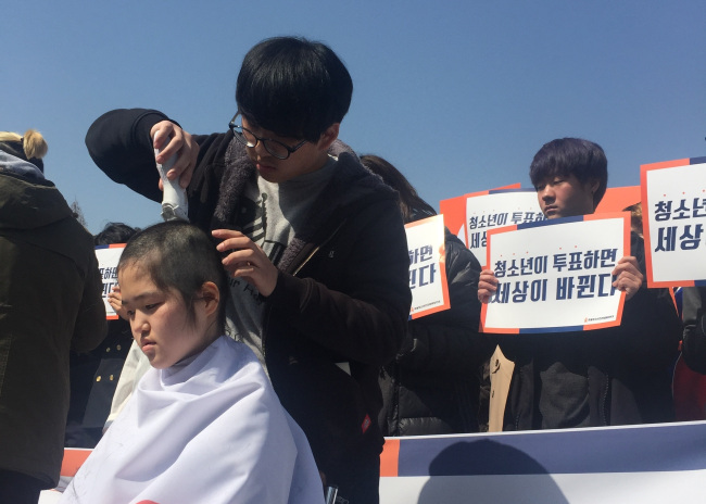 Teenager Kim Jeong-min (left) gets her head shaved bald in protest against the current voting age that only allows those 19 or older to cast ballots. (Claire Lee/The Korea Herald)