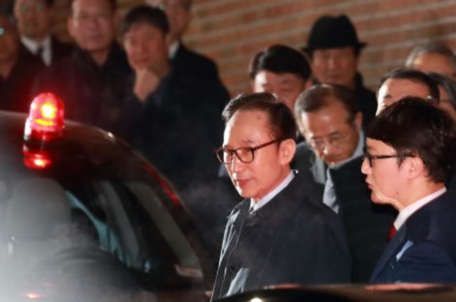 Former President Lee Myung-bak is escorted by prosecution officials from his house to a vehicle that will take him to a Seoul detention center on March 23. (Yonhap)