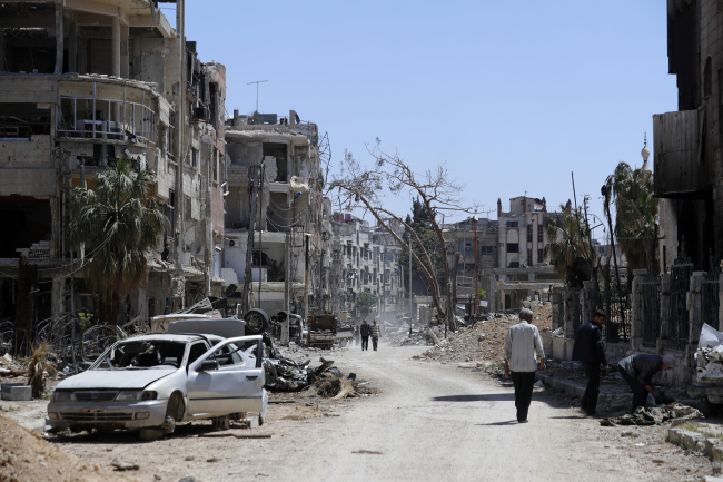Syrians walk through destruction in the town of Douma, the site of a suspected chemical weapons attack, near Damascus, Syria, Monday, April 16, 2018. (AP-Yonhap)