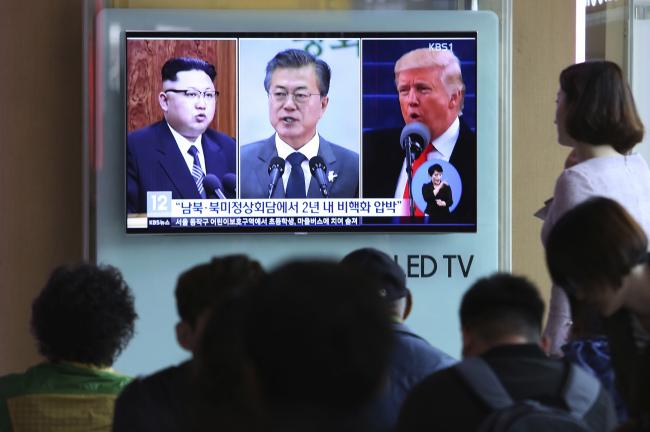 People watch a TV screen showing file footage of US President Donald Trump (right), South Korean President Moon Jae-in and North Korean leader Kim Jong Un (left), during a news program at the Seoul Railway Station in Seoul, South Korea, on Wednesday, April 18, 2018. (AP-Yonhap)