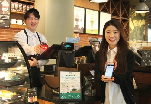 In this undated photo provided by Starbucks Coffee Korea Co., the local unit of the U.S. coffee giant, models pose for a photo at its outlet in Seoul to advertise the test operation of cashless stores in South Korea starting April 23. (Yonhap)