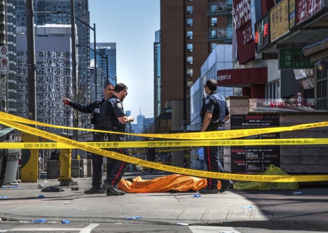 Police officers stand by a covered body in Toronto after a van mounted a sidewalk and crashed into a crowd of pedestrians on Monday, April 23. (AP)