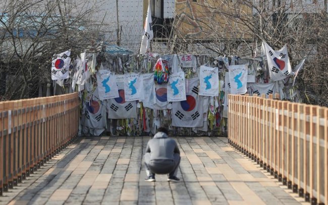 A man takes photographs near the wire fence decorated with national flags, unification flags and ribbons carrying messages wishing for reunification of the two Koreas at the Imjingak Pavilion in Paju, South Korea on Jan. 19. (AP)