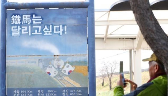 In this photo taken April 27, a man takes a photo of a bulletin that reads "The Steelhorse Wants to Run!" at a train stop no longer in use in a city in Gangwon Province near the border with North Korea. (Yonhap)