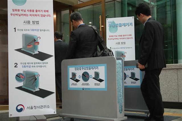 비가 내린 2일 오전 서울 세종로 정부서울청사에 출근하는 공무원들이 일회용 우산 비닐 씌우개 대신 친환경 우산 빗물 제거기를 사용하고 있다. 서울청사관리소는 일회용 비닐 사용을 줄이기 위해 이날부터 우산빗물제거기를 설치했다.  ［연합뉴스］
