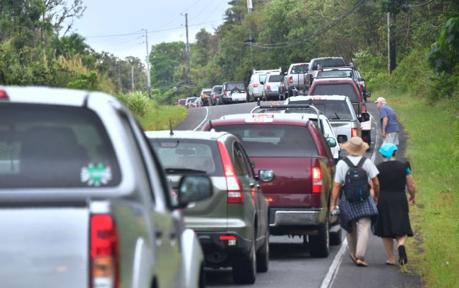 eilani Estates residents Guineverve and Matthew Underwood walk beside a long convoy of vehicles awaiting re-entry to their homes to gather belongings near the town of Pahoa on Hawaii's Big Island on May 7, 2018, after the residents were forced to evacuate following recent earthquakes and concern over toxic sulphur dioxide. (AFP-Yonhap)