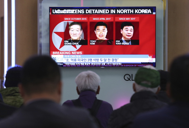 In this May 3, 2018 photo, people watch a TV news report screen showing portraits of three Americans, Kim Dong-chul (left), Tony Kim and Kim Hak-song (right), detained in the North Korea, at the Seoul Railway Station in Seoul. (AP-Yonhap)
