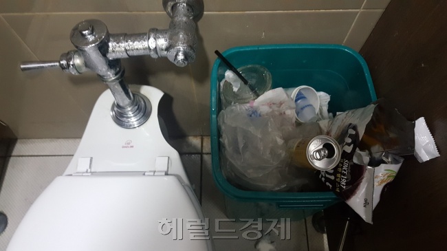 화장실 휴지통에 일회용 커피잔, 과자 봉지, 비닐봉지 등이 버려져있는 모습.