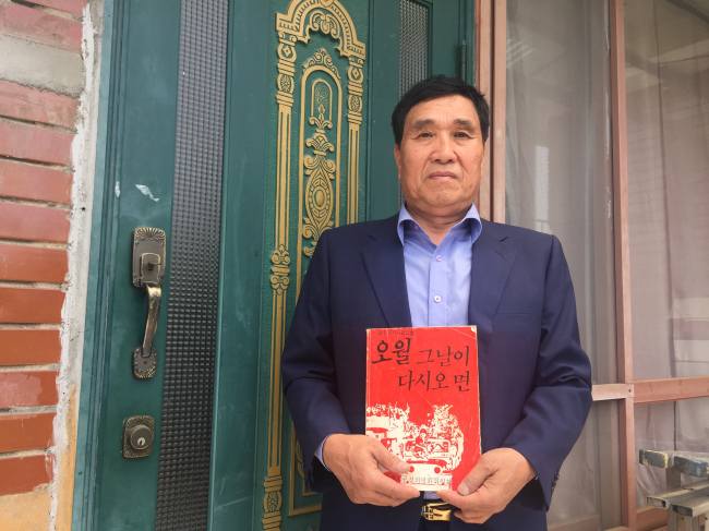 Kim Dae-yoon poses with a book that contains photographs of victims during the 1980 Gwangju Democratization Movement, which he purchased a few days after the 10-day deadly crackdown, in front of his home house in Gwangju, Monday. (Claire Lee/The Korea Herald)