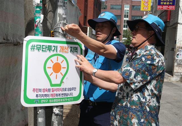 유종필(오른쪽) 관악구청장이 무단투기보안관과 전신주에 더덕더덕 붙어있는 각종 전단지를 떼어낸뒤 무단투기 개선지역 팻말을 붙이고 있다.