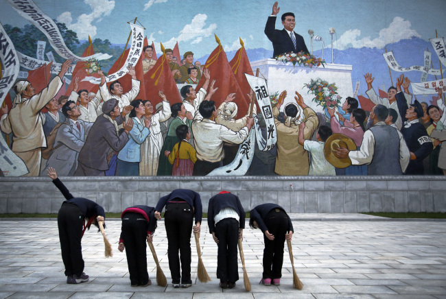 School girls holding brooms bow to pay their respects toward a mural that depicts the late North Korean leader Kim Il-sung delivering a speech, before sweeping the area surrounding the mural. (AP)