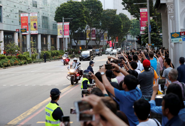 People take photographs while police vehicles escort the motorcade of North Korean leader Kim Jong-un as it makes its way to the Istana. (Reuters-Yonhap)