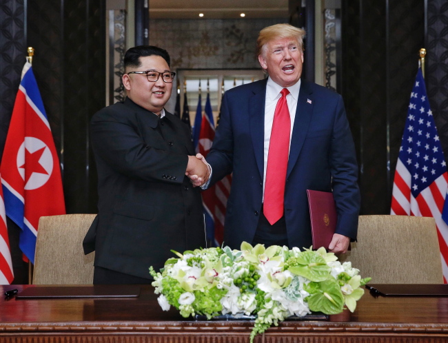 US President Donald Trump (R) and North Korean Chairmain Kim Jong-un (L) shake hands after signing a document during their historic DPRK-US summit, at the Capella Hotel on Sentosa Island, Singapore on Tuesday. (Yonhap)