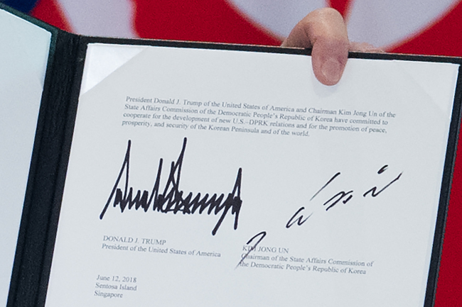 The signatures of US President Donald Trump (L) and North Korea's leader Kim Jong Un (R) are seen on a document held up by Trump following a signing ceremony during their historic US-North Korea summit, at the Capella Hotel on Sentosa island in Singapore on Tuesday. (AFP-Yonhap)