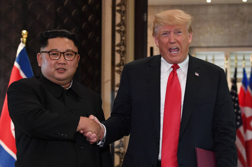 US President Donald Trump (R) and North Korea's leader Kim Jong Un shake hands following a signing ceremony during their historic US-North Korea summit, at the Capella Hotel on Sentosa island in Singapore on June 12, 2018. Donald Trump and Kim Jong Un became on June 12 the first sitting US and North Korean leaders to meet, shake hands and negotiate to end a decades-old nuclear stand-off. / AFP PHOTO