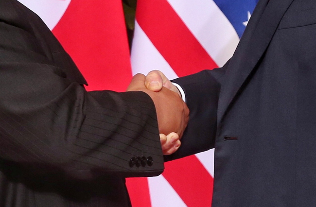 US President Donald Trump (R) and North Korean leader Kim Jong-un (L) shake hands at the start of a historic summit at the Capella Hotel on Sentosa Island, Singapore on Tuesday. (EPA-Yonhap)