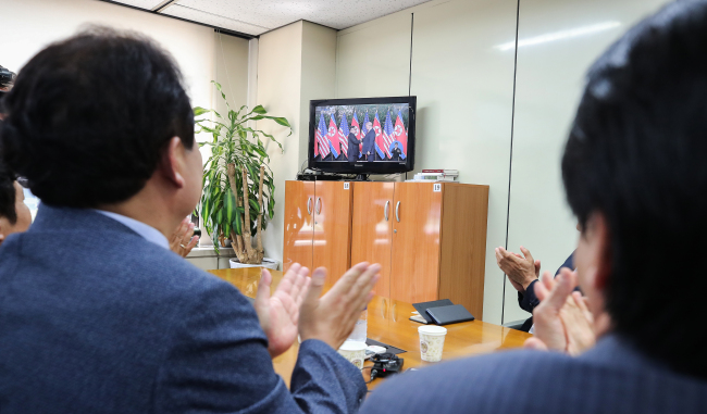 Officials of a corporate meeting on the Kaesong Industrial Complex, under the Korea Federation of SMEs in Seoul, clap as they watch US President Donald Trump and North Korea's leader Kim Jong-un shake hands at their summit in Singapore, Tuesday. (Yonhap)
