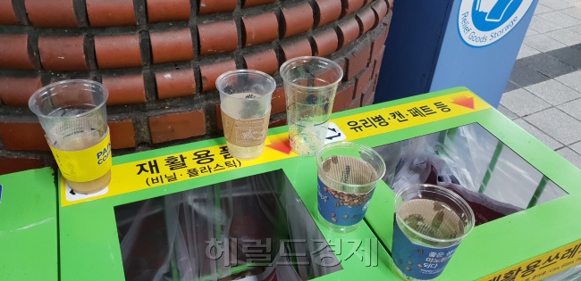 분리수거함 위에 버려져 있는 일회용 컵들(왼쪽사진). 환경미화원이 음료수컵에 남은 액체를 분리하고 있는 모습