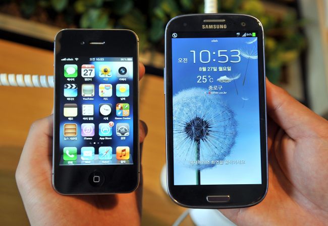 In this file photo taken on August 26, 2012, an employee shows an Apple's iPhone 4s (left) and a Samsung's Galaxy S3 at a mobile phone shop in Seoul. Apple and Samsung have ended a years-long patent battle over copied iPhone design with an undisclosed settlement, according to a US court filing on June 27, 2018. The world's two biggest smartphone makers reached a truce in their seven-year-old court battle a month after a federal court jury ordered Samsung to pay Apple some $539 million for copying patented iPhone features. (AFP-Yonhap)