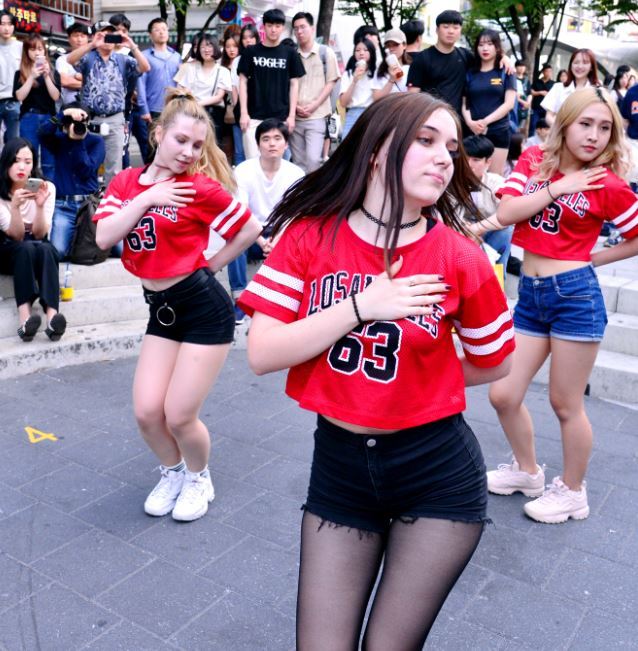 Hongdae busking scene near Hongik University with a Korean street performer and gathered audience in the pedestrian zone, capturing the outdoor performance culture that has served as a launchpad for Korean indie musicians and dance crews