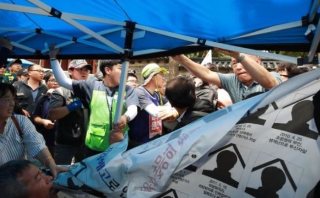 Mourners of a laid-off worker who took his own life last month, nine years after losing his job at Ssangyong Motors, are attacked by elderly conservative Koreans at the memorial site of the late laborer set up in front of the main gate of Deoksugung in central Seoul on Wednesday. (Yonhap)