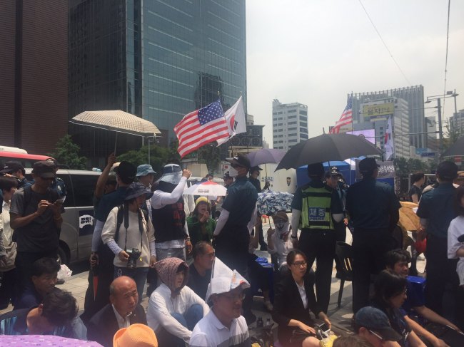 Elderly conservative Koreans (waving American and Korean flags) shout at mourners at the memorial site for a late laid-off worker in central Seoul, Wednesday. (Claire Lee/ the korea Herald)