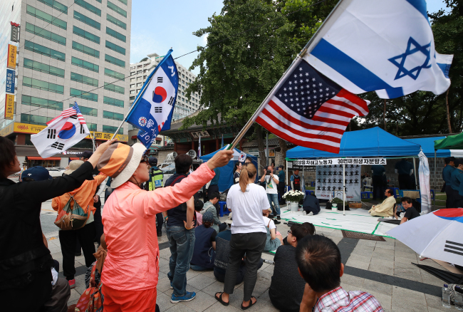 Elderly conservative Koreans(waving South Korean and American flags) insult mourners at a memorial site held for a late laid-off worker who took his own life after losing his job at Ssangyong Motors nine years ago, in central Seoul on Wednesday.(Yonhap)