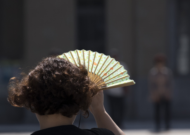 A South Korean woman covers her face with a fan from the sun as she spends time outdoors in central Seoul on Tuesday (Yonhap).