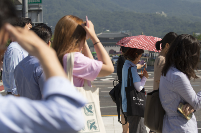 Koreans cover their heads from the sun in a 35 degrees celsius weather in central Seoul, Tuesday. (Yonhap)