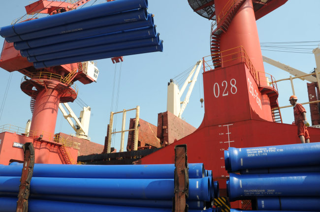 A worker looks on as a crane lifts steel pipes for export at a port in Lianyungang, Jiangsu province, China July 15, 2018. (Reuters)