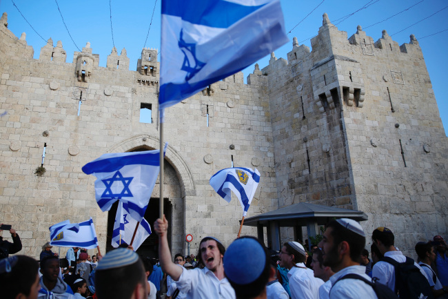 In this Sunday, May 13, 2018, file photo, Israelis wave national flags outside the Old City's Damascus Gate, in Jerusalem. Israel's parliament has approved a controversial piece of legislation that defines the country as the nation-state of the Jewish people. Opponents and rights groups have criticized the legislation, warning that it will sideline minorities such as the country's Arabs. (Yonhap)