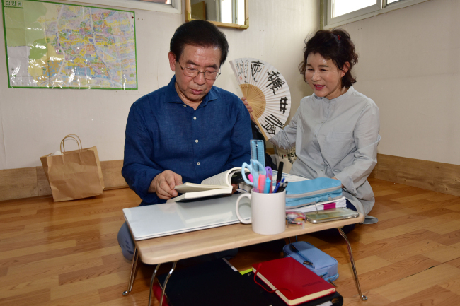 Seoul Mayor Park Won-soon (left) reads at his new, temporary residence -- a rooftop dwelling in Samyang-dong of Gangbuk-gu district of Seoul -- along with his wife, Kang Nan-hee (right). (Yonhap)