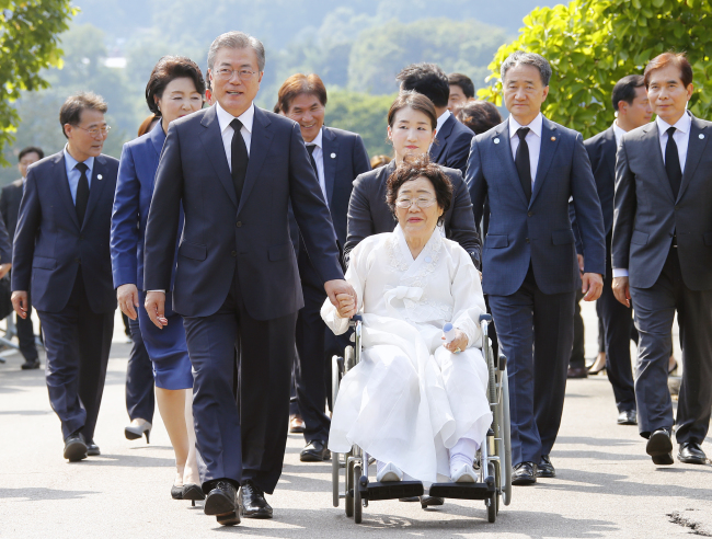 South Korean President Moon Jae-in (right) holds hands with a Korean survivor of Japan's military sex slavery during World War II, during a special ceremony to honor the victims on Tuesday. (Yonhap)