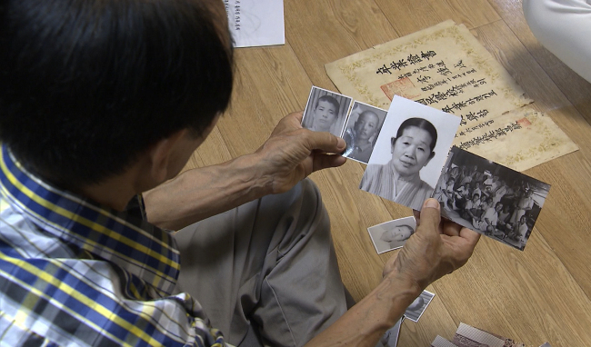 In this file photo dated Aug. 15, 77-year-old Lee Soo-nam holds up photos of his family left in North Korea. (Yonhap)