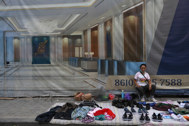 <YONHAP PHOTO-2487> epa06948455 A Chinese woman selling clothes and shoes by the roadside is seen in front of a banner showing a luxury apartment in the Central Business District in Beijing, China, 13 August 2018 (issued 14 August 2018). China's economy appears to be showing signs of further cooling as tougher US tariffs looms and investment in the first seven months of the year slow to a record low, according to data released by the National Bureau of Statistics on 14 August 2018. Fixed-asset investment growth slowed more than expected to 5.5 percent in the January-July period from a year earlier, while retail sales missed expectations at 8.8 percent in July from a year earlier. EPA/HOW HWEE YOUNG/2018-08-14 14:53:33/ <저작권자 ⓒ 1980-2018 ㈜연합뉴스. 무단 전재 재배포 금지.>
<YONHAP PHOTO-2487> epa06948455 A Chinese woman selling clothes and shoes by the roadside is seen in front of a banner showing a luxury apartment in the Central Business District in Beijing, China, 13 August 2018 (issued 14 August 2018). China's economy appears to be showing signs of further cooling as tougher US tariffs looms and investment in the first seven months of the year slow to a record low, according to data released by the National Bureau of Statistics on 14 August 2018. Fixed-asset investment growth slowed more than expected to 5.5 percent in the January-July period from a year earlier, while retail sales missed expectations at 8.8 percent in July from a year earlier. EPA/HOW HWEE YOUNG/2018-08-14 14:53:33/ <저작권자 ⓒ 1980-2018 ㈜연합뉴스. 무단 전재 재배포 금지.>