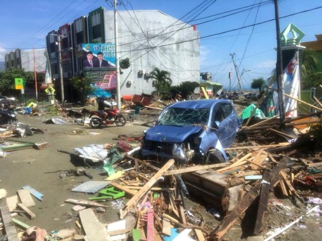 A motorbike passes the wreckage of a car following earthquakes and a tsunami in Palu, Central Sulawesi, Indonesia, Sunday, Sept. 30. (AP)