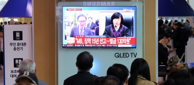 Seoul residents watch the sentencing of ex-President Lee Myung-bak at Seoul station on Oct. 5. (Yonhap)