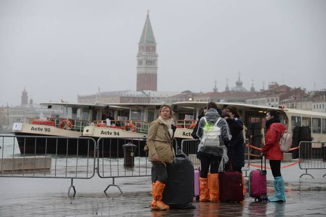 People stand in a flooded street of Venice, Italy, backdropped by St. Marks Basilica bell tower, Monday, Oct. 29, as, according to city officials, 70 percent of the lagoon city has been flooded by waters rising 149 centimeters (more than 58 1/2 inches) above sea level. (AP)