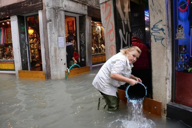 A woman removes water from a shop in a flooded street of Venice, Italy, Monday, Oct. 29. (AP)