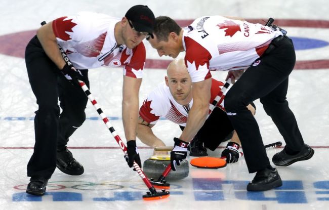 Canada's Ryan Fry delivers the rock while Ryan Harnden, left, and E.J. Harnden, right, sweep the ice during the men's curling match against the United States at the 2014 Winter Olympics, Sunday, Feb. 16, 2014, in Sochi, Russia. (AP)
