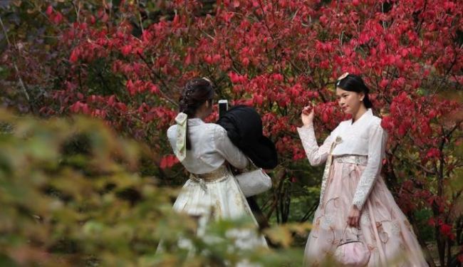 In this file photo, taken on Oct. 23, 2018, tourists wearing the traditional Korean costume hanbok take pictures against a background of maples at Deoksu Palace in Seoul. (Yonhap)