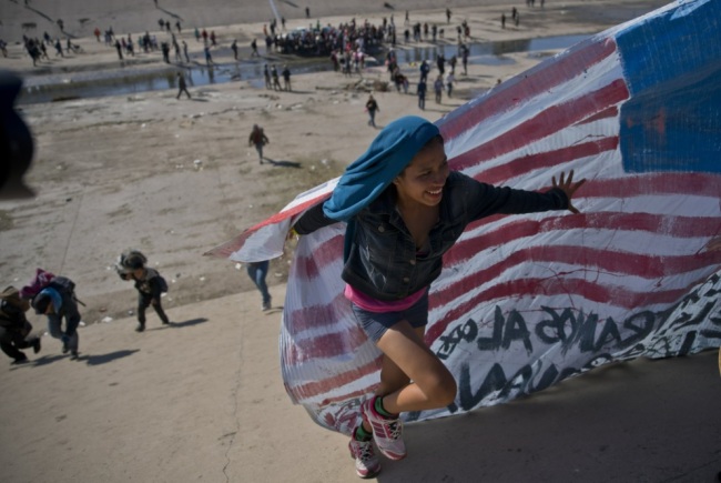 A migrant woman helps carry a handmade US flag up the riverbank at the Mexico-US border after getting past Mexican police at the Chaparral border crossing in Tijuana, Mexico, Sunday, Nov. 25, 2018, as a group of migrants tries to reach the US. The mayor of Tijuana has declared a humanitarian crisis in his border city and says that he has asked the United Nations for aid to deal with the approximately 5,000 Central American migrants who have arrived in the city. (AP)