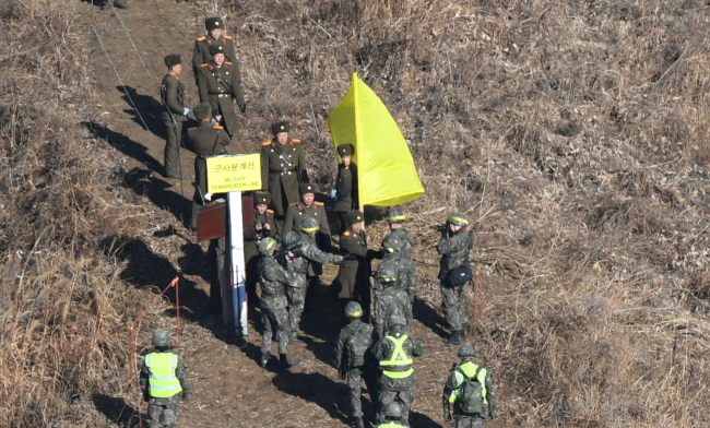 The two Koreas' military inspection teams shake hands at a cross-border region marked with a yellow flag Wednesday. Yonhap