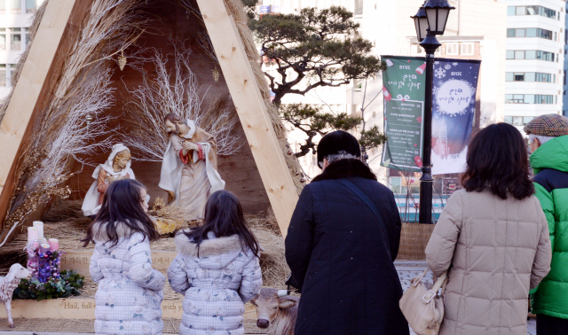 24일 크리스마스 이브를 맞아 명동성당 밖 마구간 말구유 조형물에 가족들이 기도를 드리고 있다. <br />정희조 기자/checho@heraldcorp.com  181224