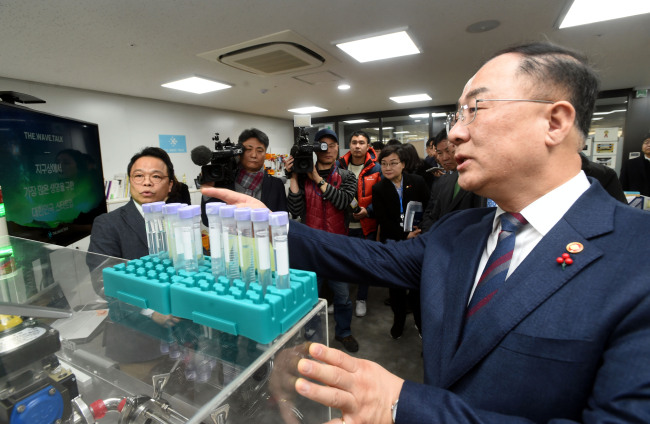 Finance Minister Hong Nam-ki is briefed on the business portfolio of a startup stationed at a local incubator for budding enterprises in Yangjae, southern Seoul, Wednesday. Yonhap
　